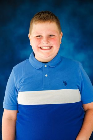 Smiling boy in blue and white U.S. Polo Assn. shirt poses for school portrait photo against blue background.
