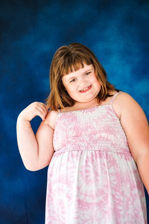 Young girl in pink sundress smiling at camera against blue studio background.
