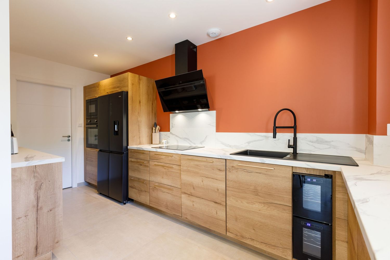 Cuisine avec des placards en bois, des appareils électroménagers noirs, des plans de travail en marbre et un mur d'accent orange.