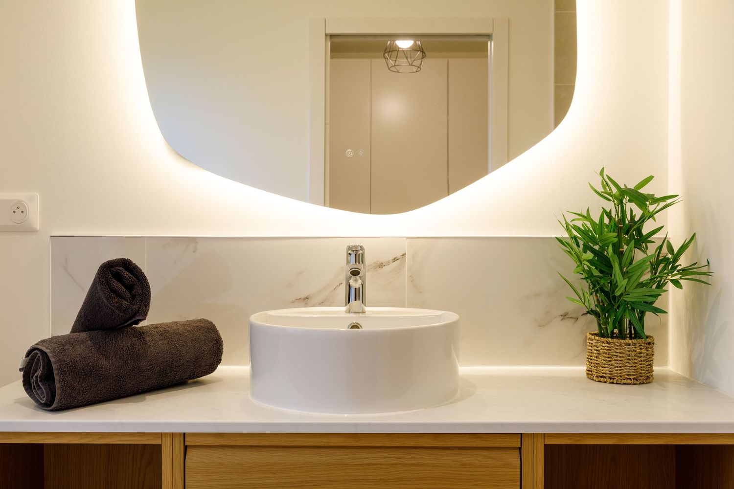 Meuble-lavabo moderne avec vasque ronde à poser, plan de toilette en marbre, miroir ovale rétroéclairé, serviettes sombres plant de bambou