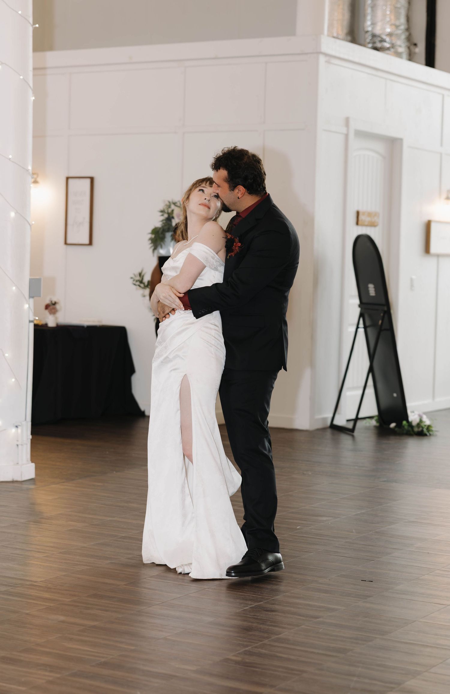 Bride and groom share an intimate first dance on a wood floor in a bright, elegant wedding venue.
