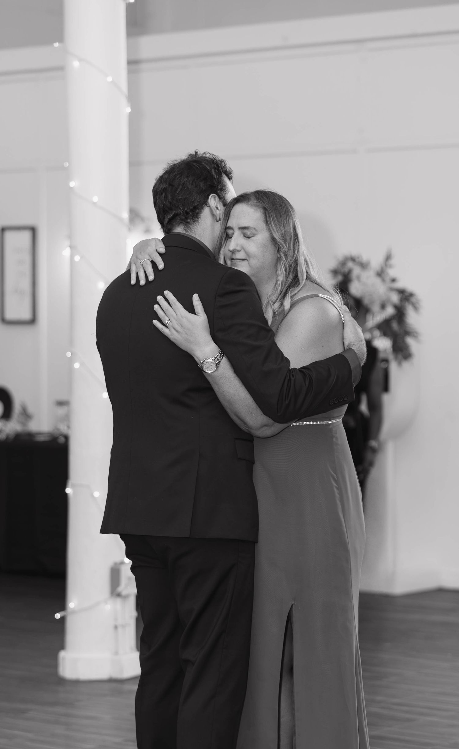Black and white photo of the groom embracing a woman in a long dress during an emotional dance at the wedding reception.