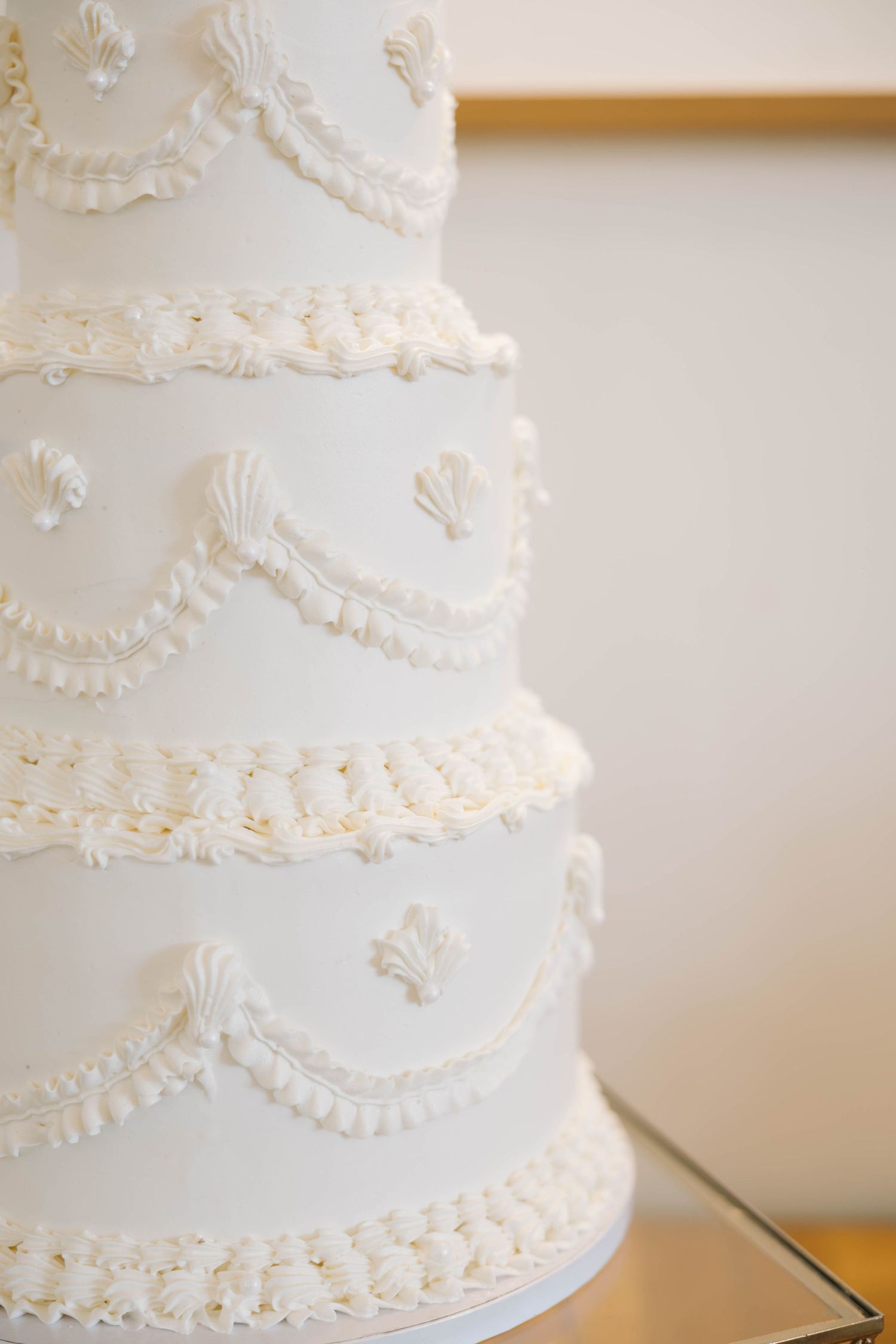 Elegant tiered white wedding cake decorated with intricate piped buttercream swags, shell details, and delicate borders.