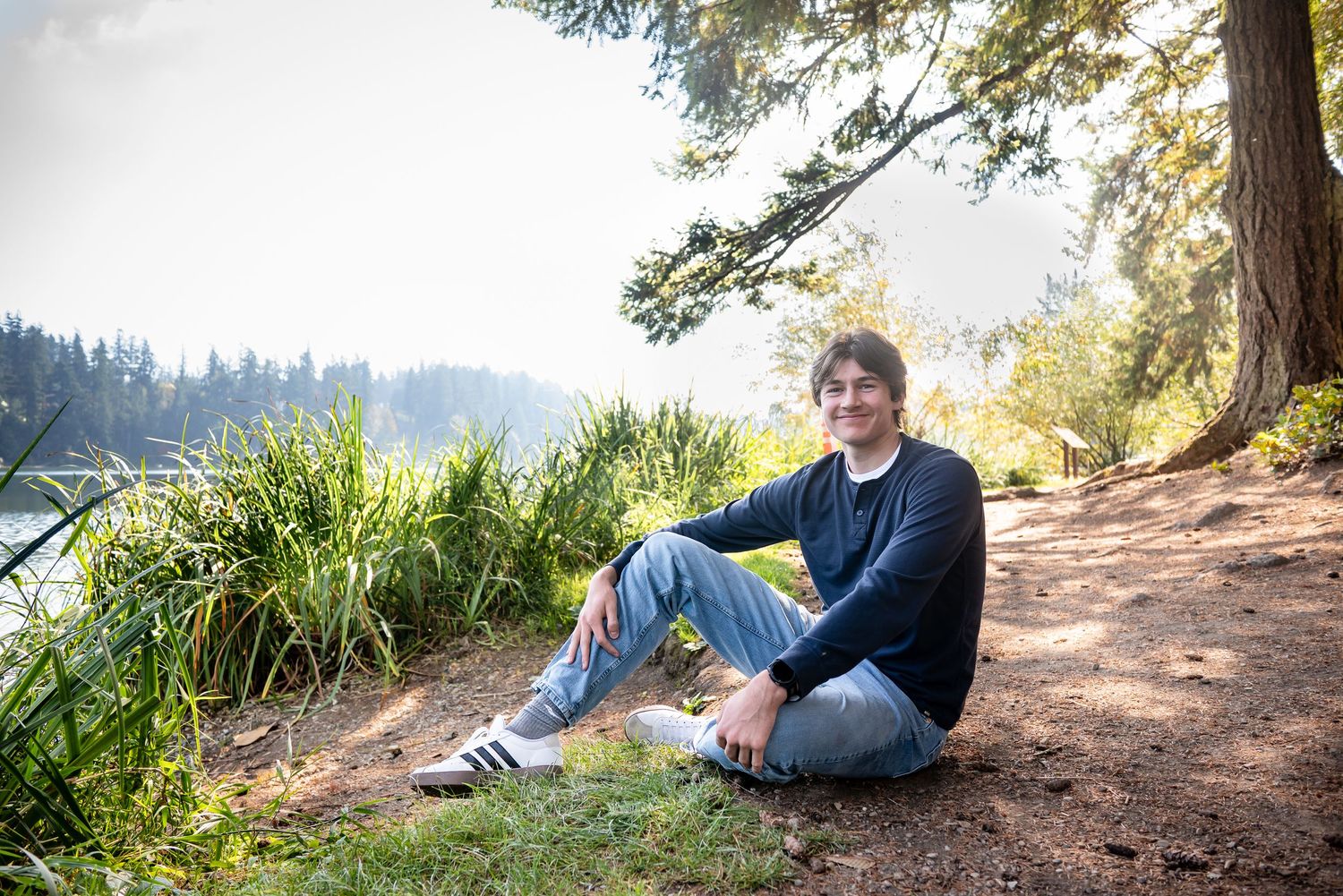 High school senior wearing a casual outfit while seated in front of leafy green foliage