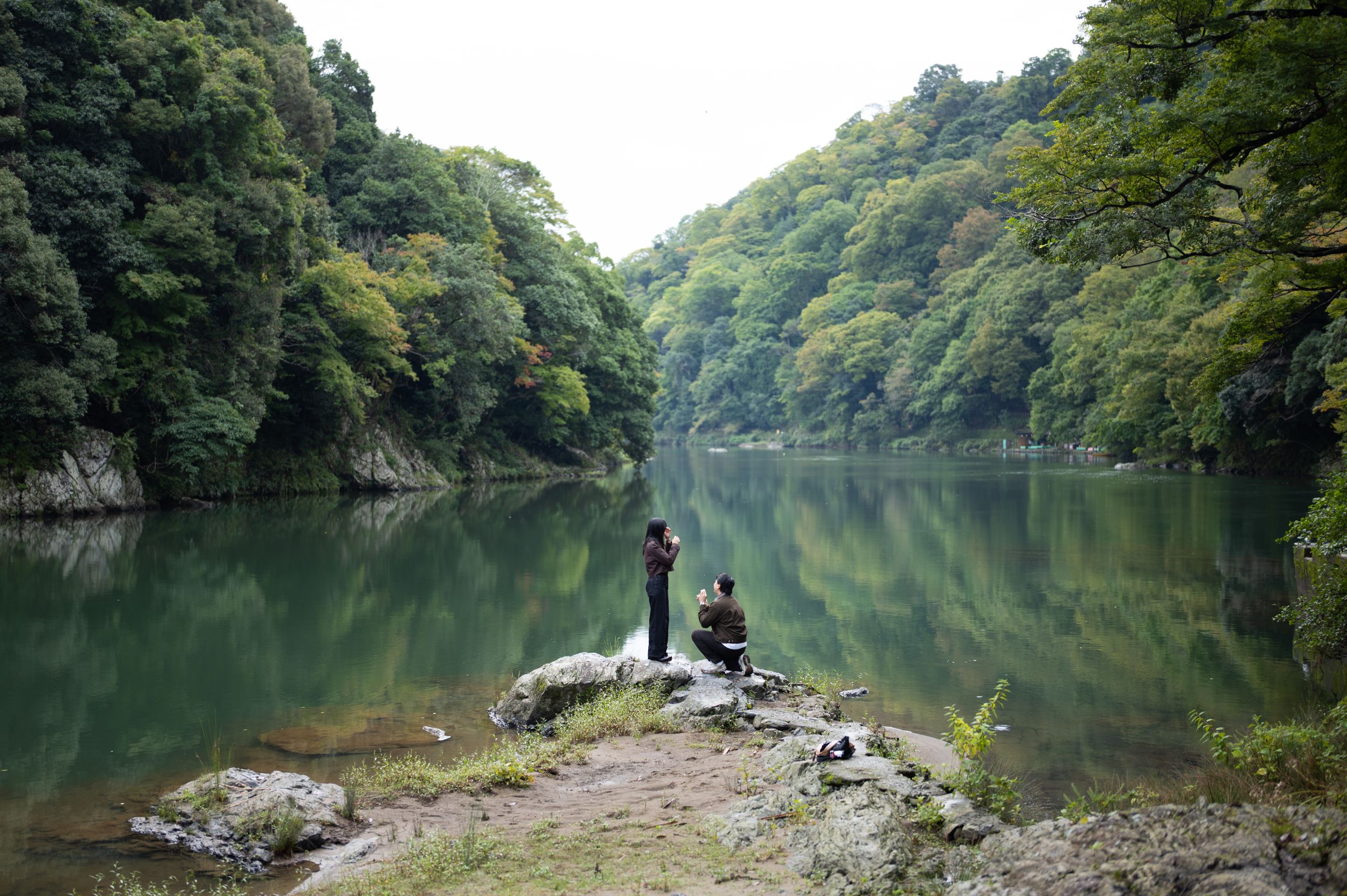 Couple standing on a wooden bridge surrounded by lush green trees in a Japanese garden.