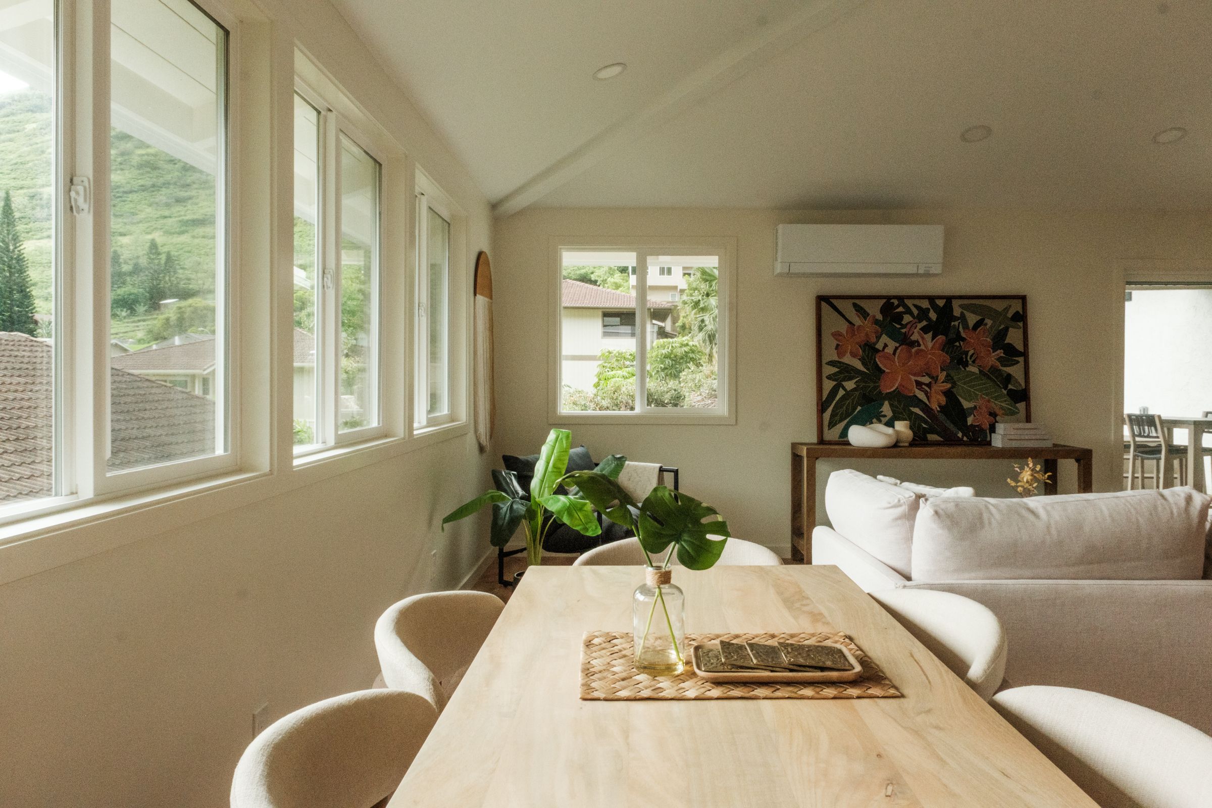 Dining room with a wood table, white chairs, and large windows bringing in natural light.