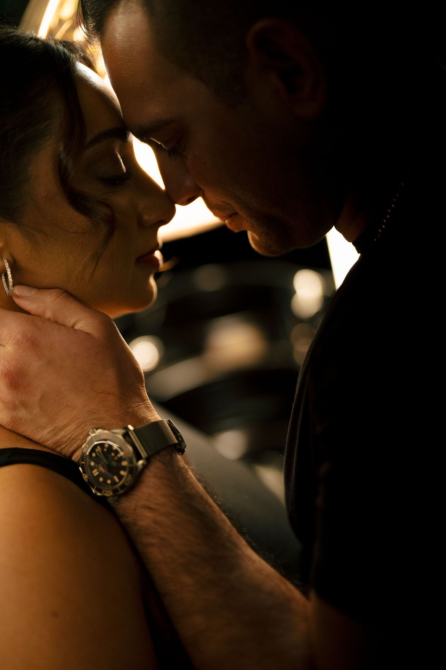A couple in formal attire walks arm-in-arm down a tree-lined urban sidewalk, captured with motion blur.