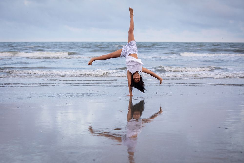 Woman performing a cartwheel on a reflective wet beach with ocean waves in the background.