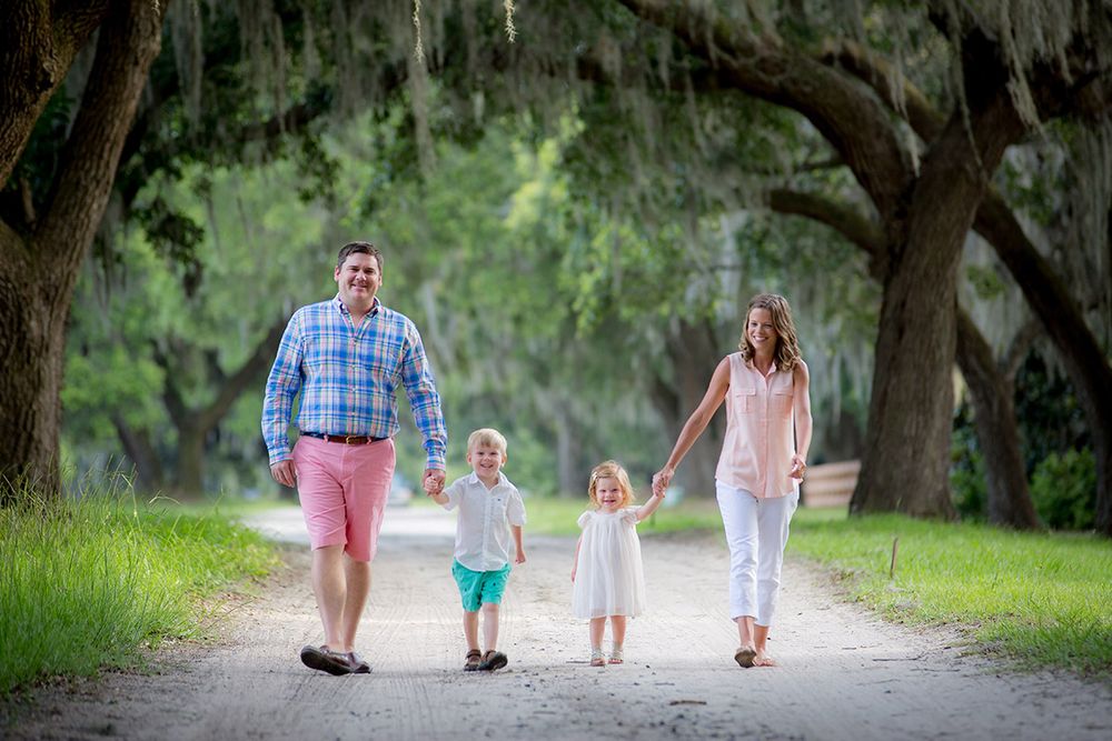 Family of four walking hand-in-hand on a scenic tree-lined path surrounded by lush greenery.