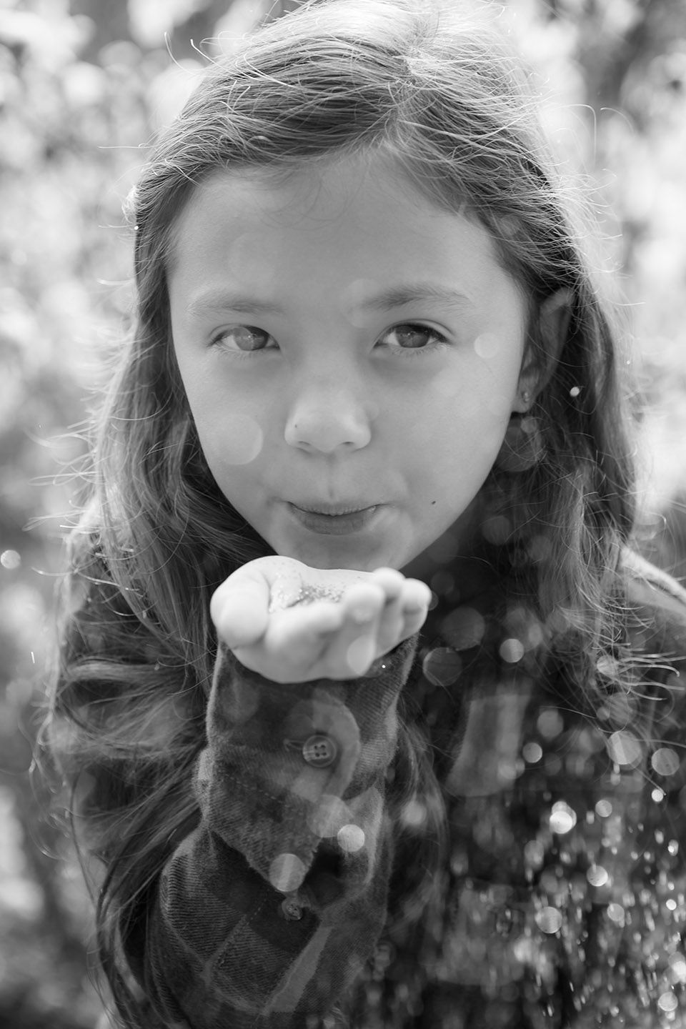 Black and white photo of a young girl blowing glitter from her hand outdoors.