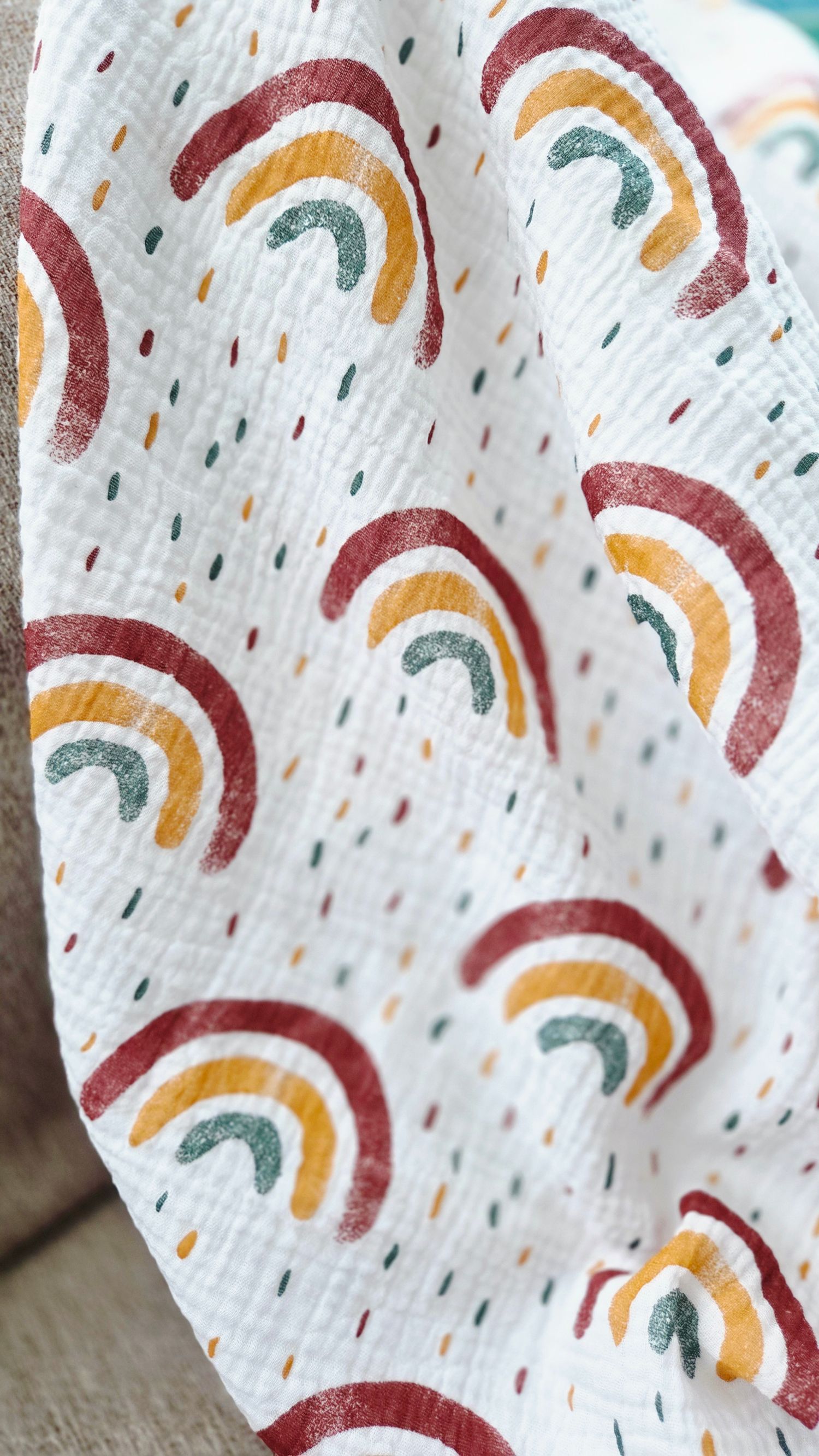 Soft white muslin fabric printed with boho rainbows in burgundy, mustard and teal, scattered with tiny confetti dots.