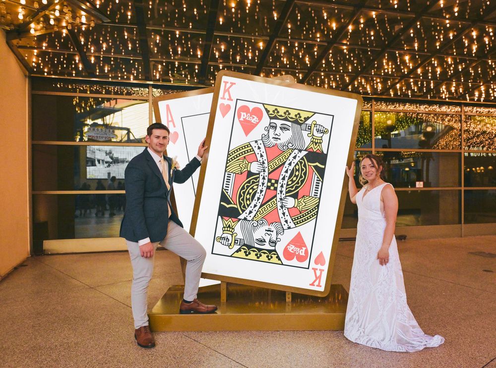 Bride and groom posing with a giant King of Hearts playing card prop at a casino-themed wedding venue.