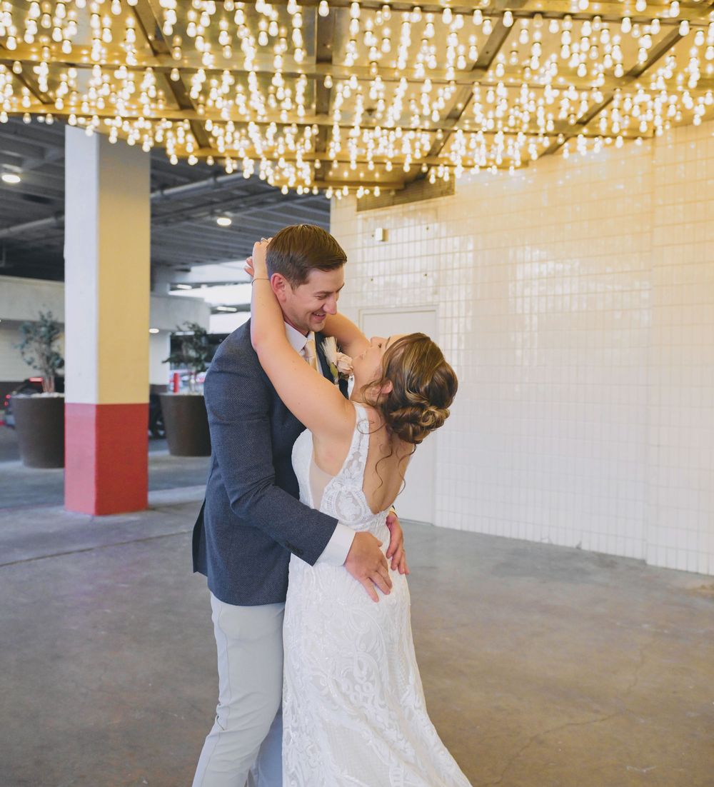 A bride and groom share their first dance under warm string lights in a modern wedding venue.