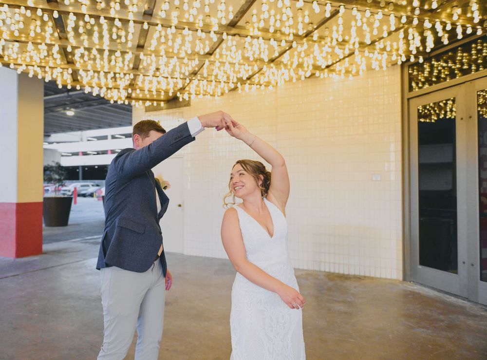 Bride and groom dancing joyfully under sparkling string lights at an elegant indoor wedding venue.