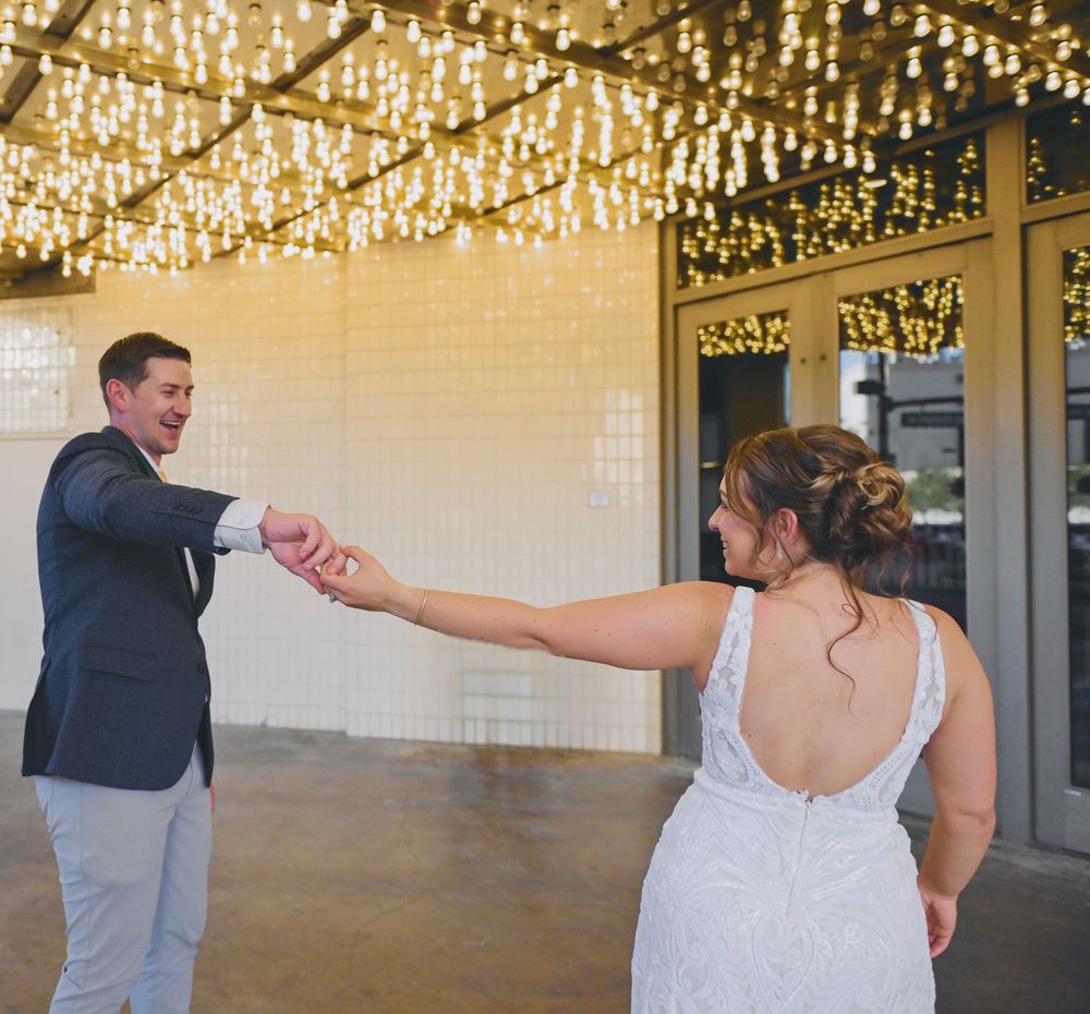 Groom spinning bride in a lace wedding dress under a canopy of hanging fairy lights.