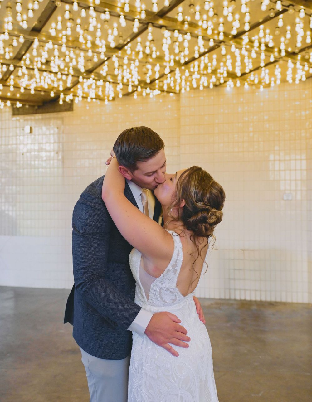 Newlyweds share their first kiss under glowing chandeliers in an elegant wedding venue.