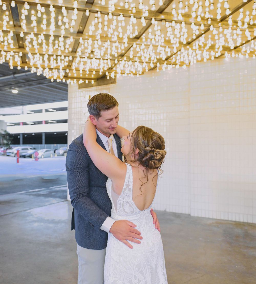 Newlyweds share romantic embrace under glowing chandelier lights at elegant wedding venue.