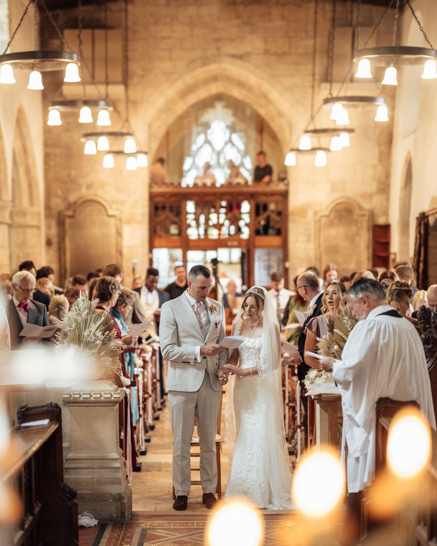 Bride and groom exchange vows at a candlelit church wedding ceremony with guests seated in wooden pews.