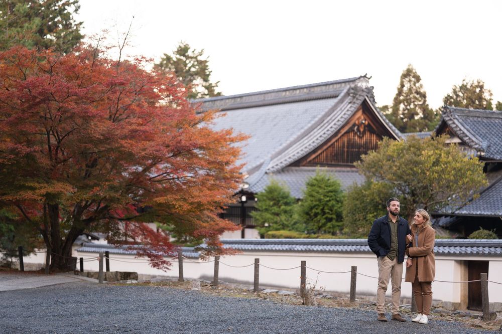 Couple standing before a traditional Japanese temple with vibrant autumn maple trees in Kyoto, Japan.