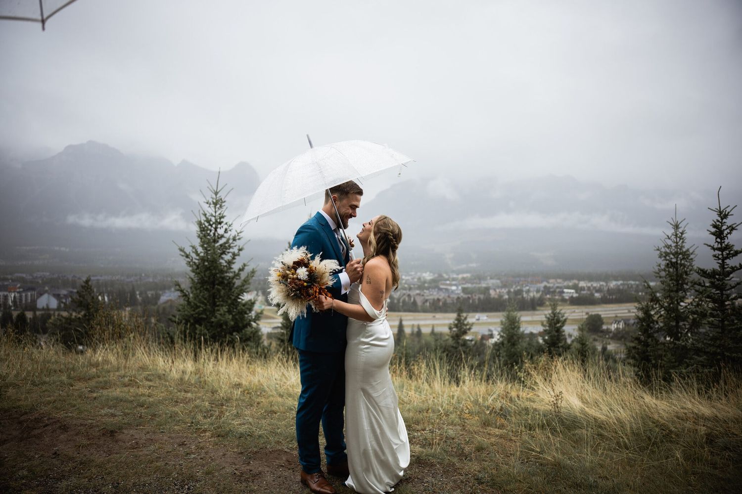 Bride and groom sharing an umbrella on a rainy mountain wedding day