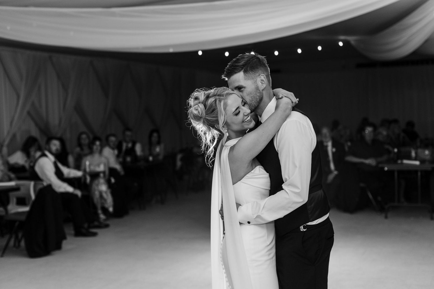 Black and white photo of a bride and groom sharing their first dance at a wedding reception.