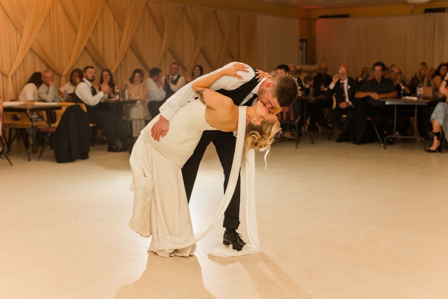 Bride and groom share a romantic dip kiss on the dance floor during their wedding reception.