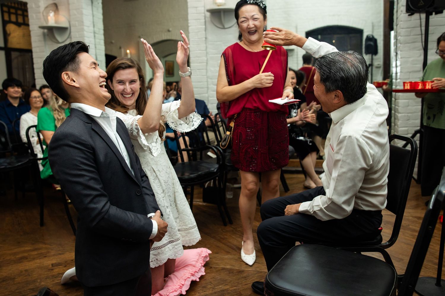 Joyful wedding reception guests laughing and clapping during a fun game, elegantly dressed in a warmly lit venue.