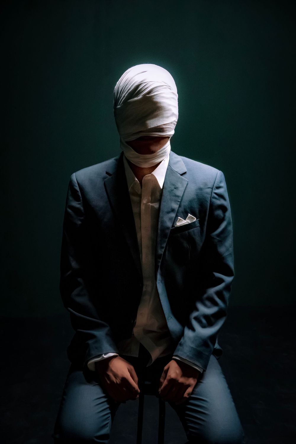 Person in suit with bandaged head sitting in dark studio, mysterious business concept photo.