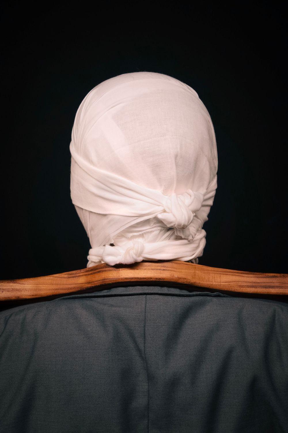 Rear view of person with white cloth-wrapped head resting on wooden yoke, dark background.