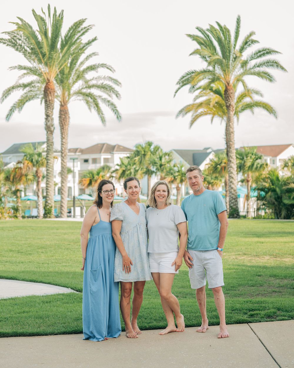 Four people posing together on green lawn with tall palm trees and resort buildings in background.