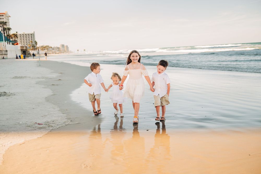 Family walking together on beach wearing coordinated white outfits at sunset.