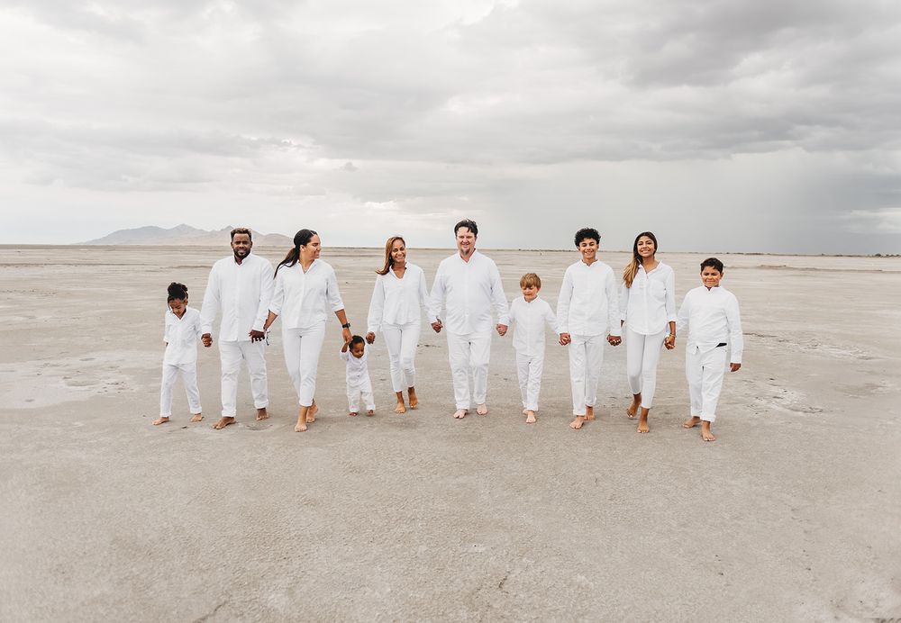 Group in all white clothing poses together on salt flats under dramatic cloudy sky.