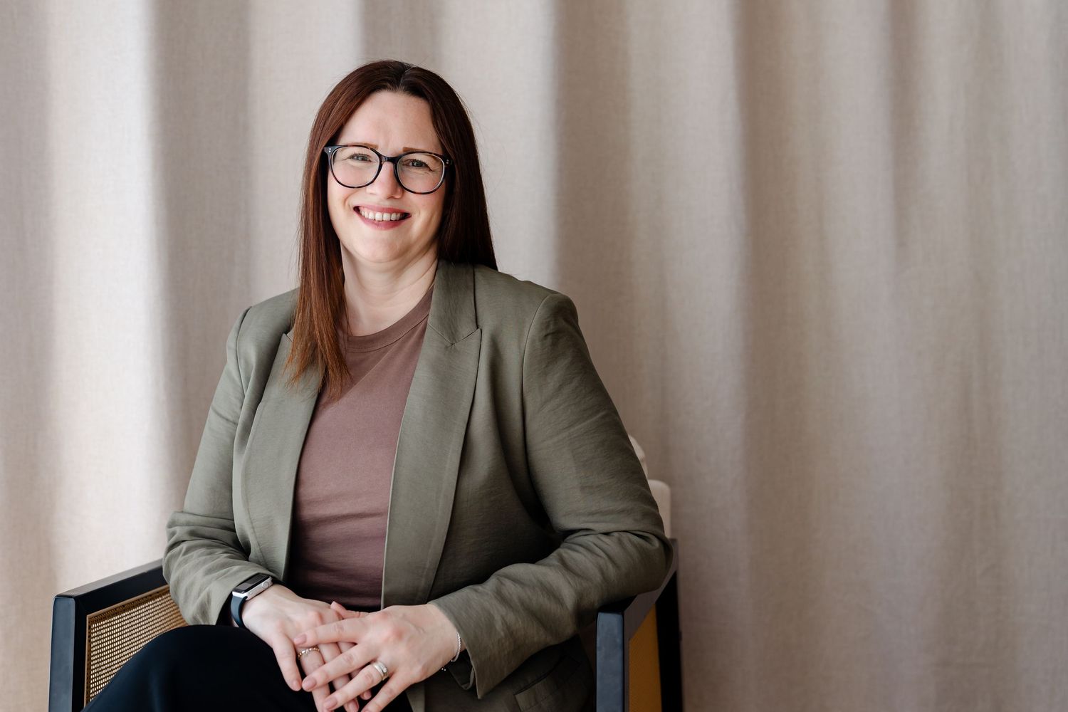 Professional woman in navy top and tan pants smiling confidently in a bright, modern office space with wooden beams.