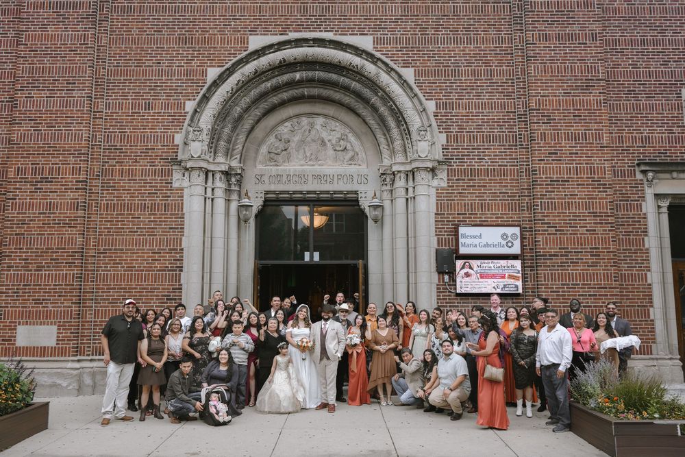 Wedding party poses outside historic brick church with ornate arched entrance after ceremony.