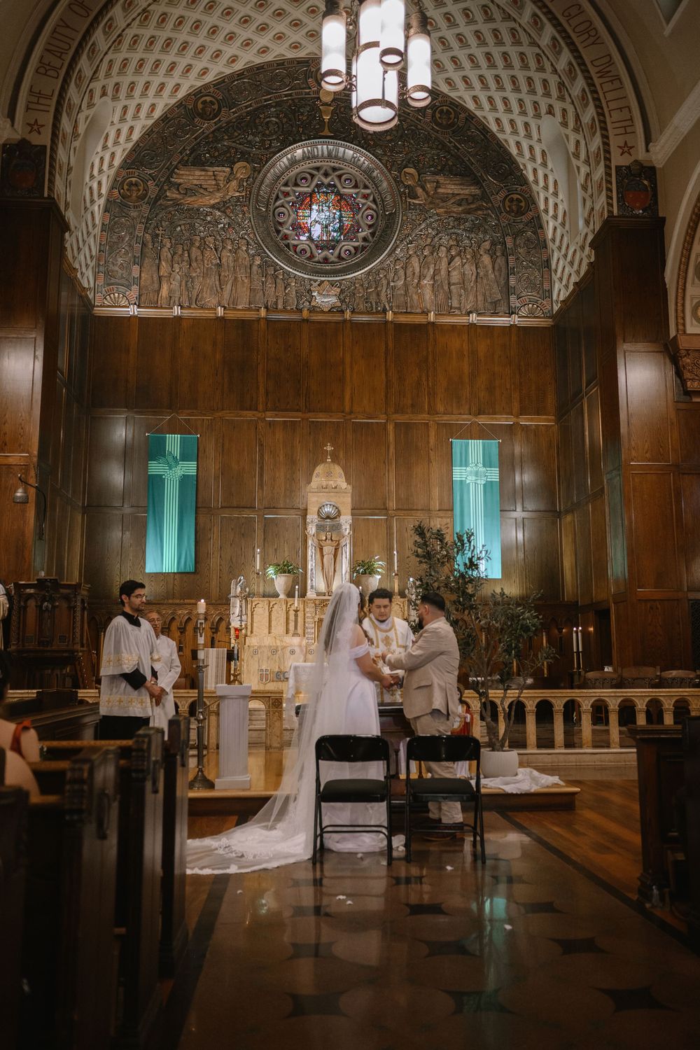 Bride and groom exchanging vows at ornate church altar with arched ceiling and stained glass windows.