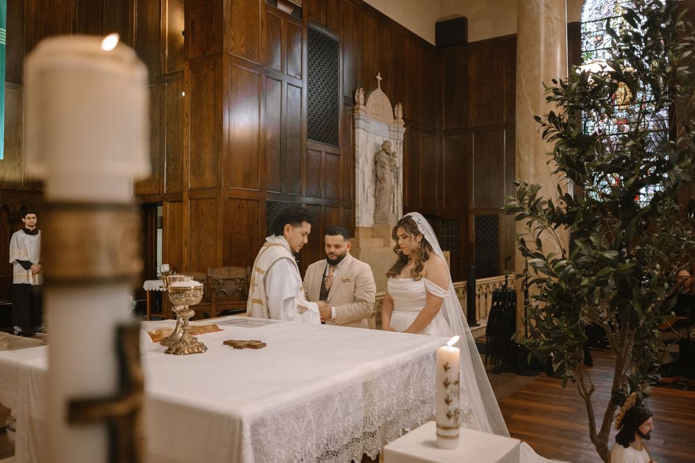 Couple exchanging vows at church altar during Catholic wedding ceremony with priest officiating.