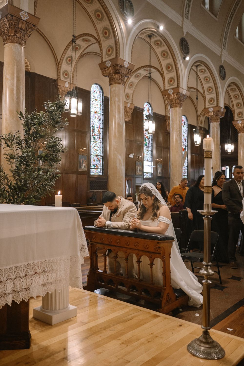 Bride and groom kneel in prayer at the altar during their wedding ceremony inside a historic Catholic church.