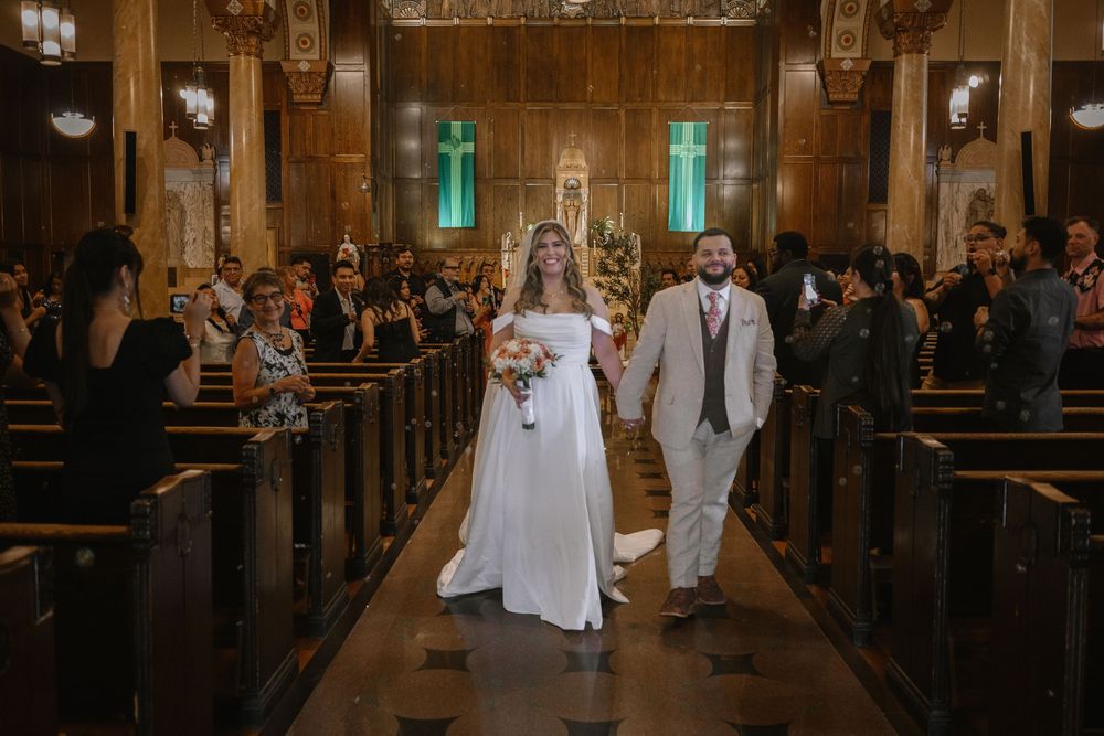 Newlyweds walk down aisle of elegant wood-paneled church as guests celebrate their marriage.