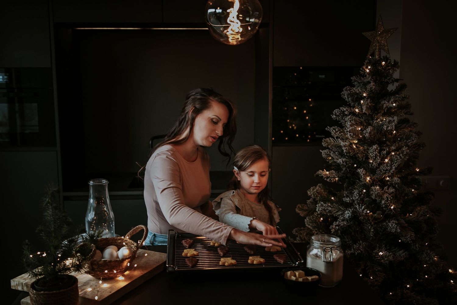 Daughter decorating cookies on a baking tray in a cozy kitchen beside Christmas tree during a family storytelling photoshoot in Utrecht.