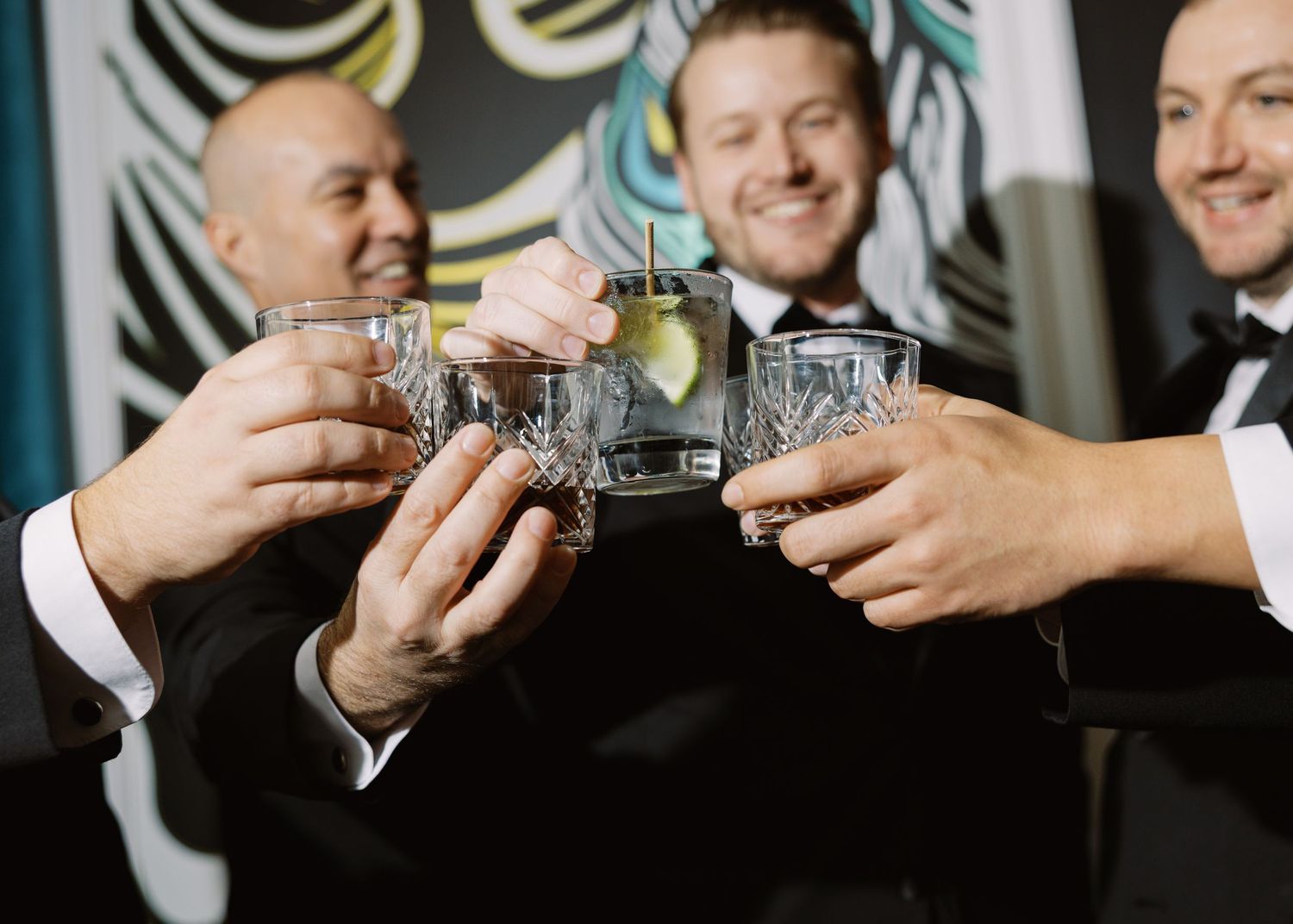 Three men in tuxedos toasting with cocktail glasses at a formal celebration.