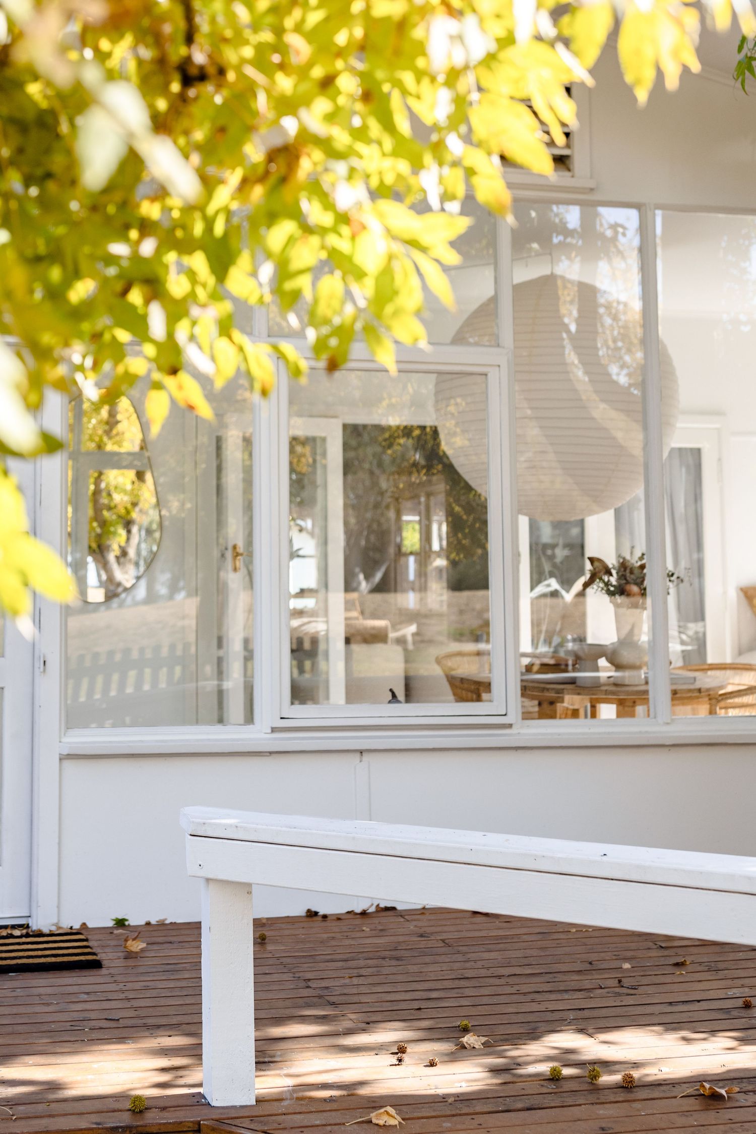 Sunlit white building exterior with wooden deck and green autumn leaves in foreground.
