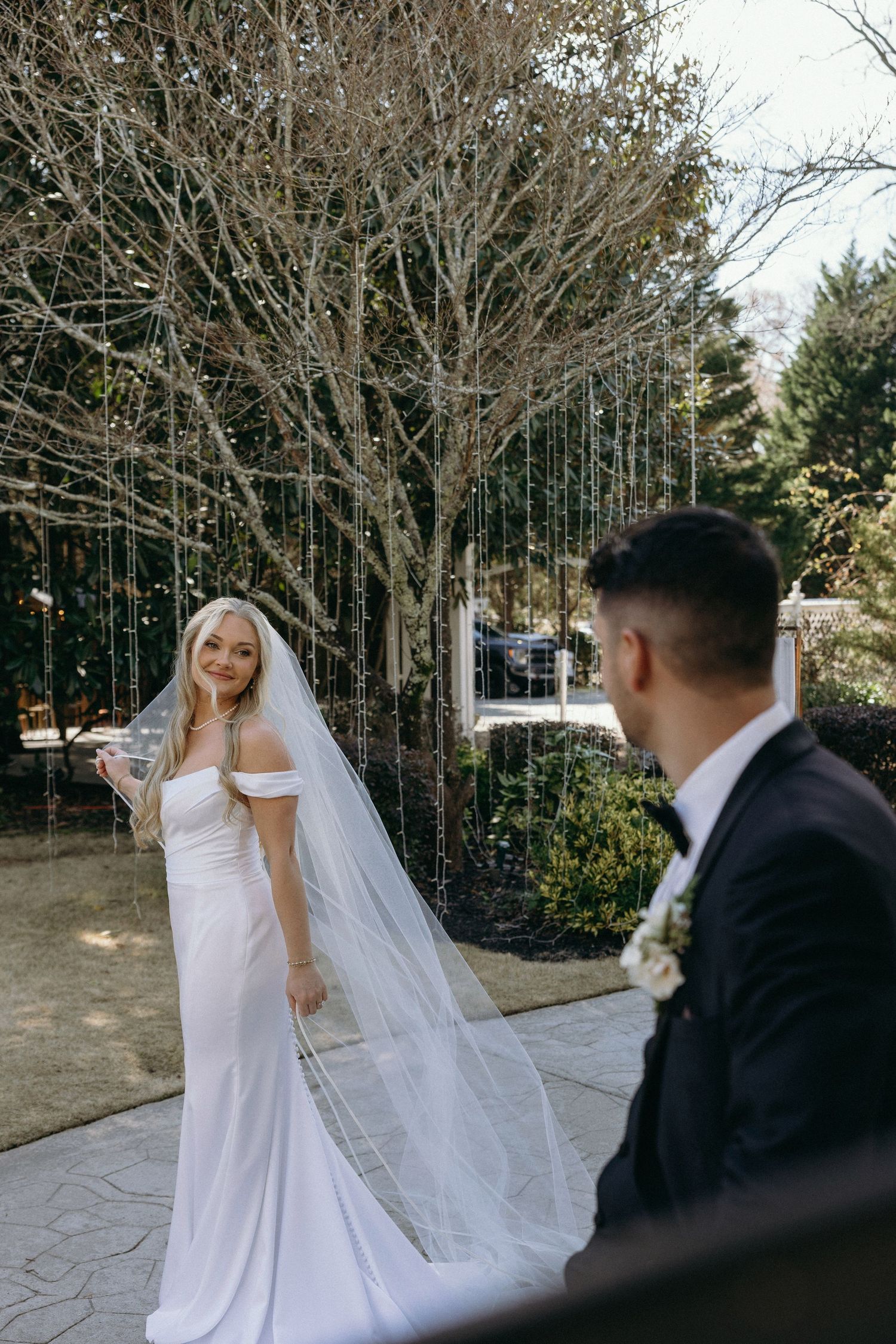 Bride in white gown and veil smiles at groom in black tuxedo during outdoor wedding ceremony at Georgia wedding venue