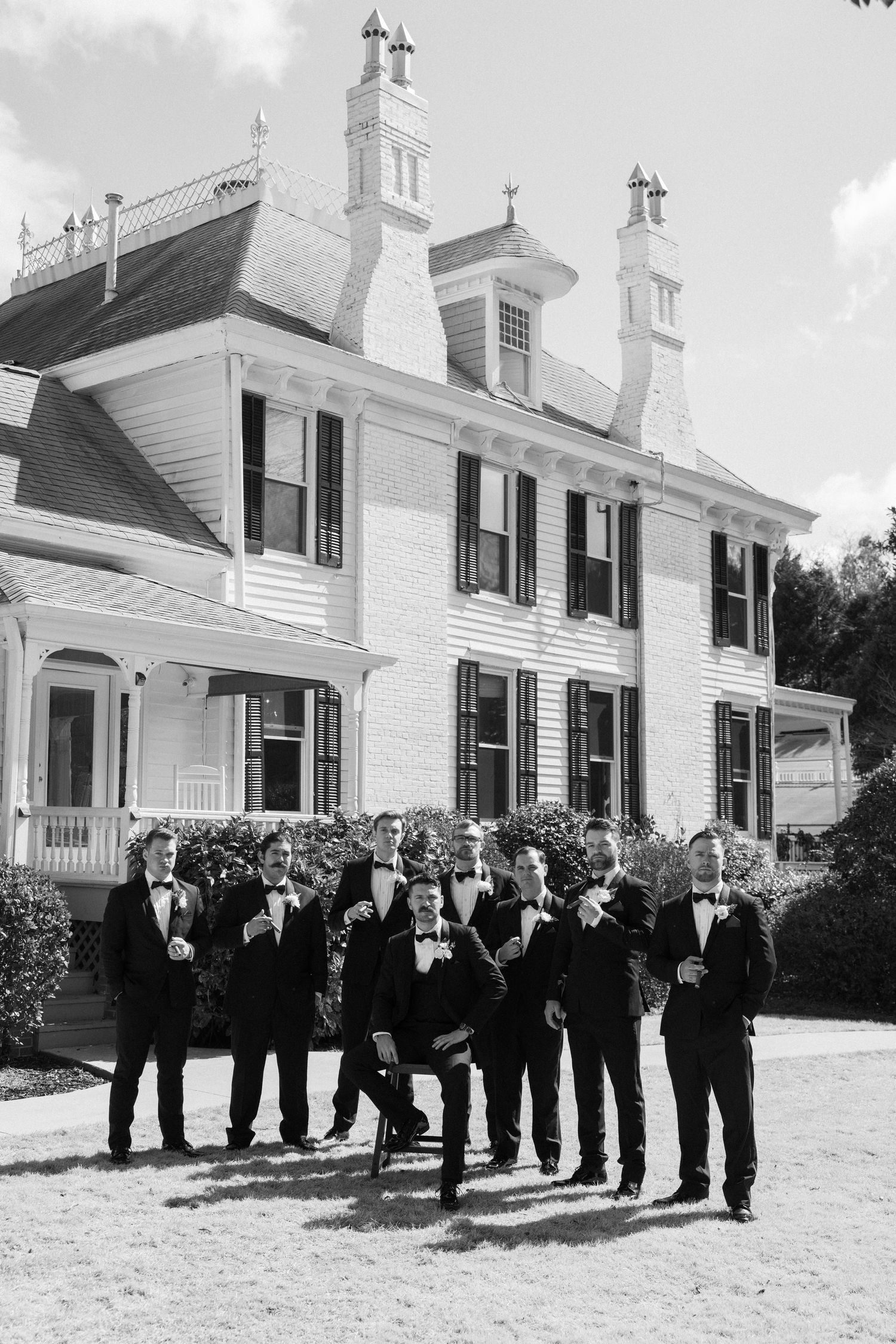 Groom and groomsmen in black tuxedos pose outside the Wildflower 301 in a black and white wedding photo.