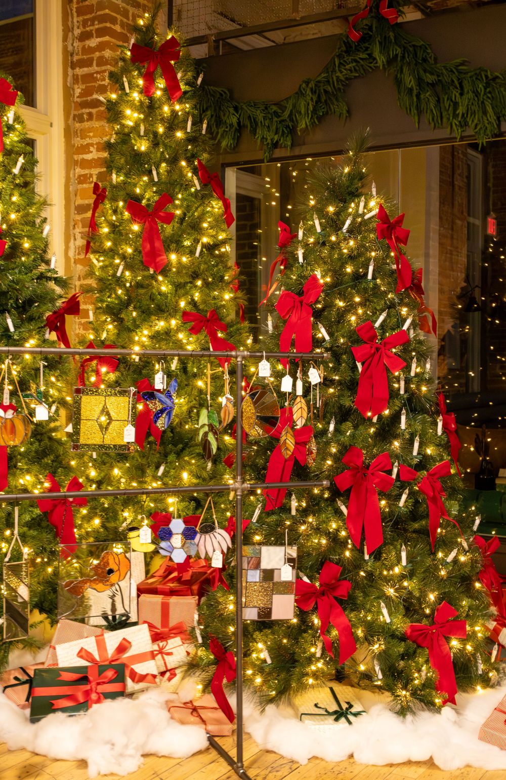 Festive Christmas trees decorated with red bows, warm lights, and colorful ornaments with wrapped gifts below.