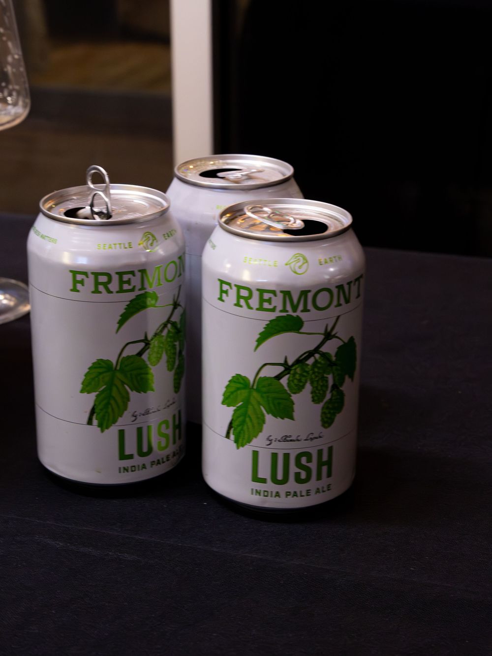Three cans of Fremont Brewing Lush India Pale Ale displayed on a dark surface.