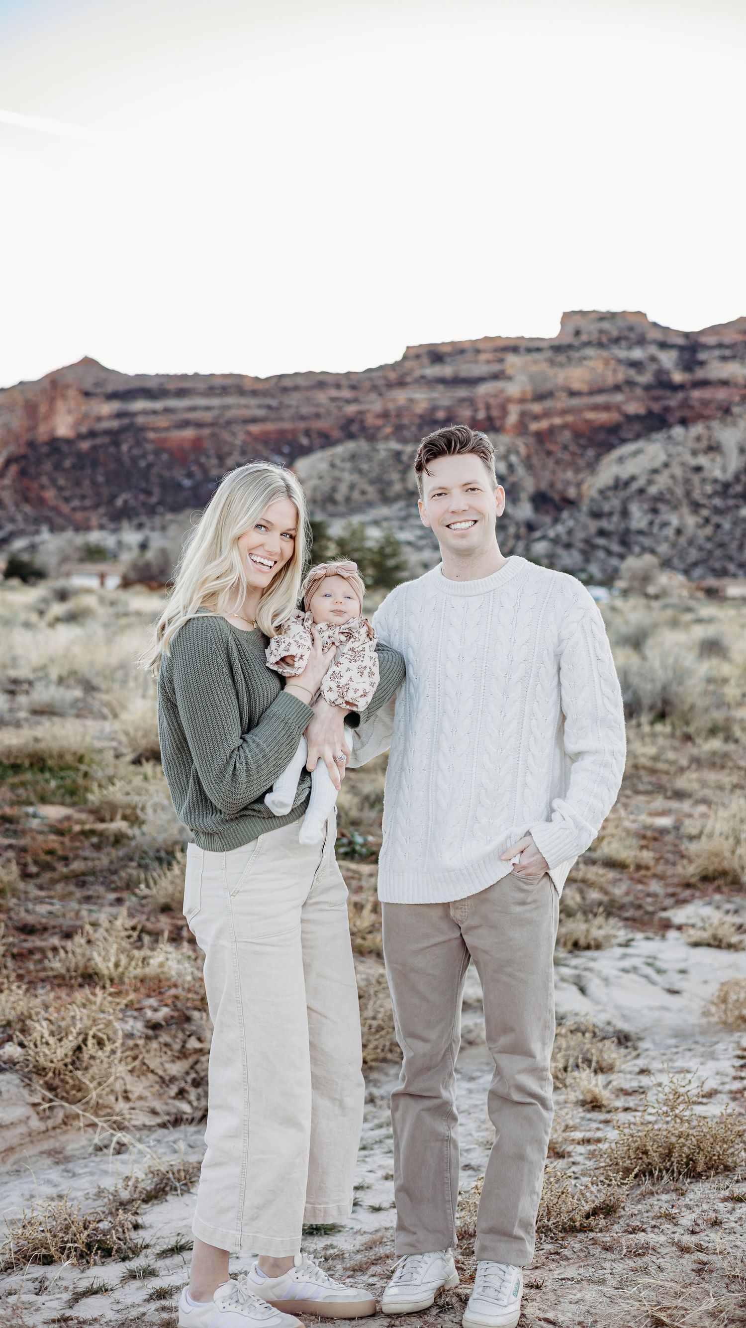 Family of seven in coordinated neutral outfits,  posing together in a desert landscape with Colorado national monument