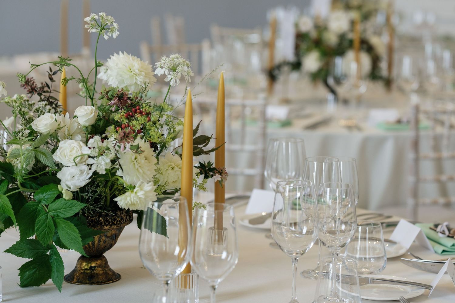 Elegant wedding table setting with white and green floral centerpiece, tall taper candles, crystal glassware and place settings.