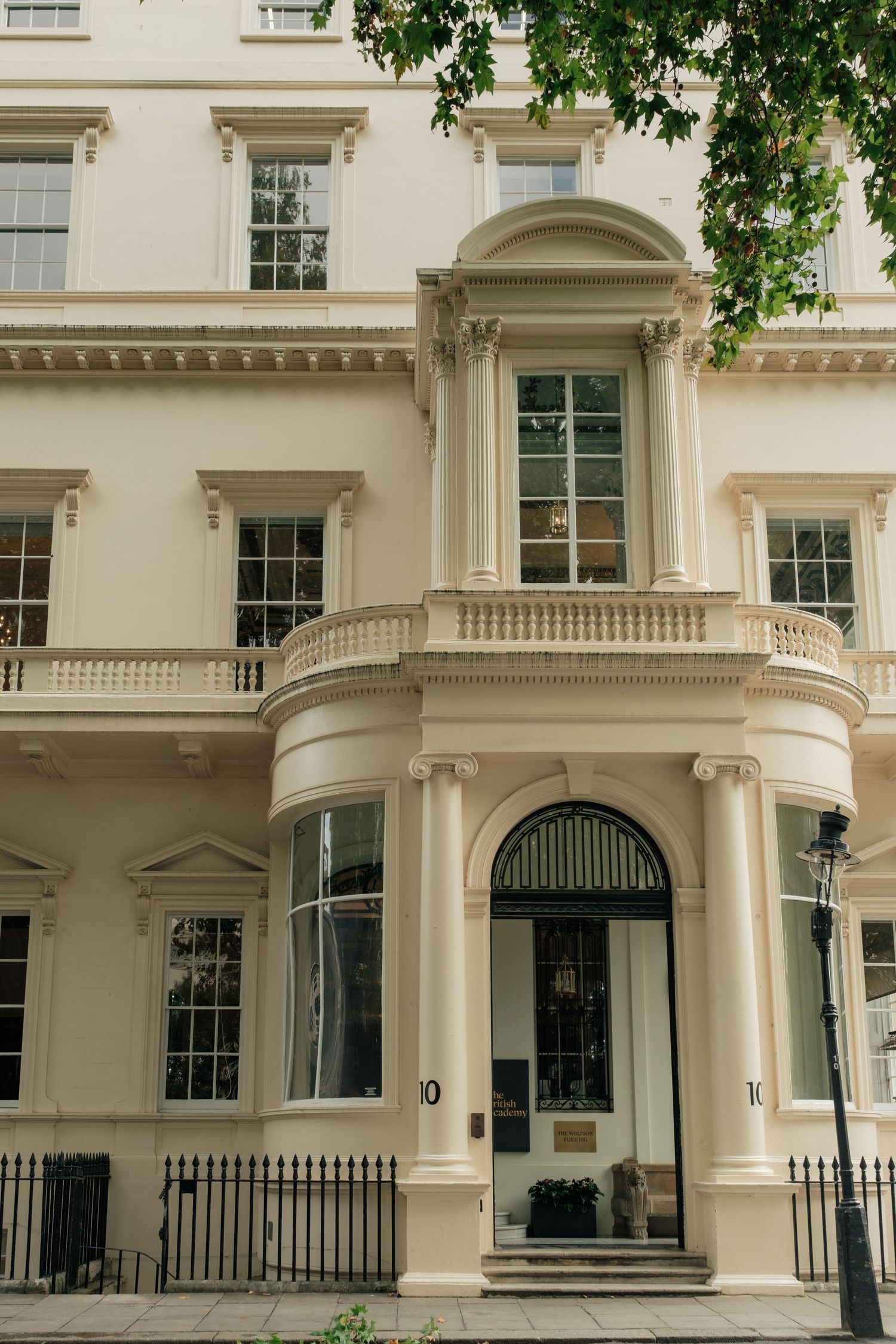 Cream-stucco Georgian townhouse with a curved bowed entrance, arched doorway, tall sash windows, balustrade balcony and black iron railings.