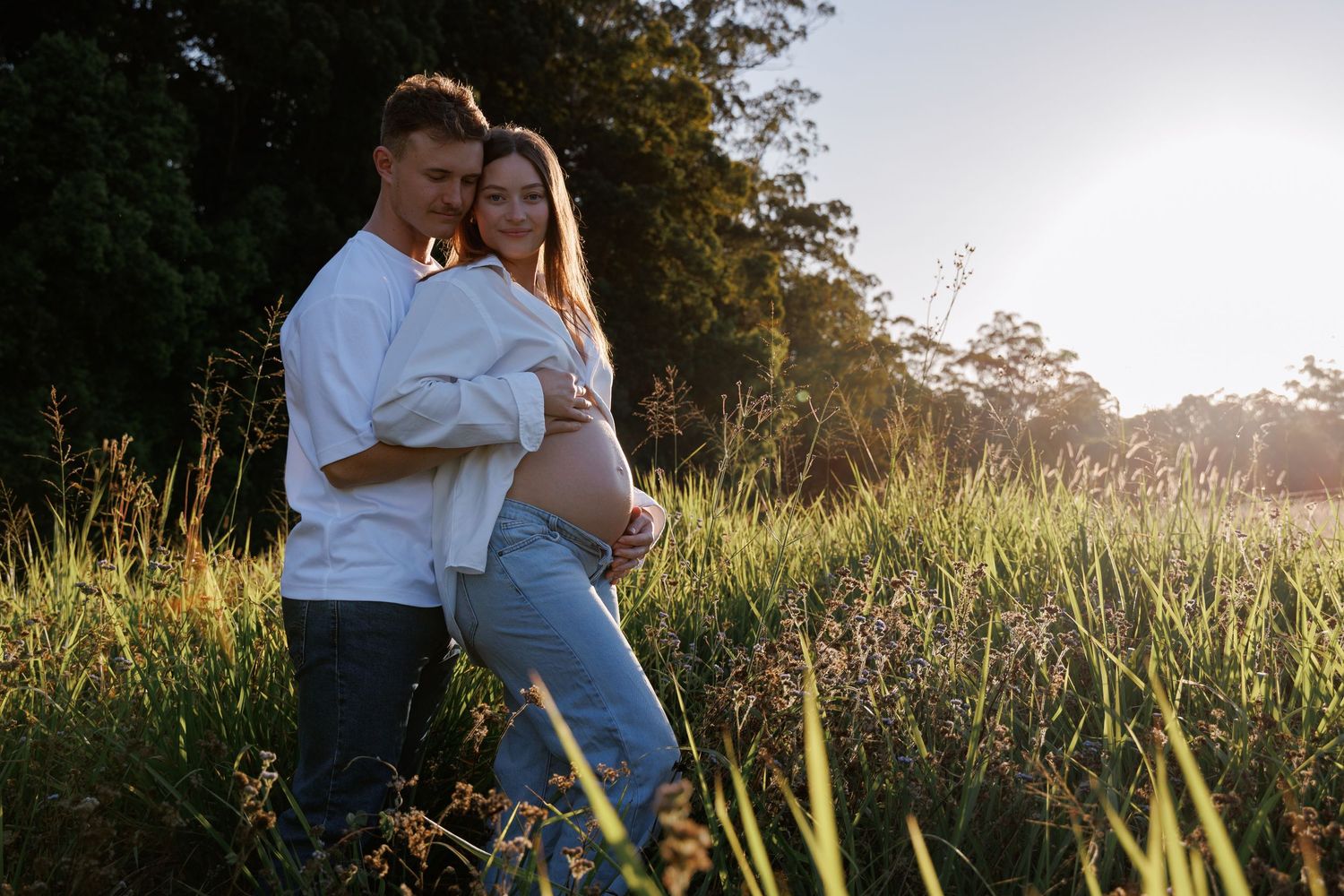 husband hugging pregnant wife in golden hour sunset rural setting