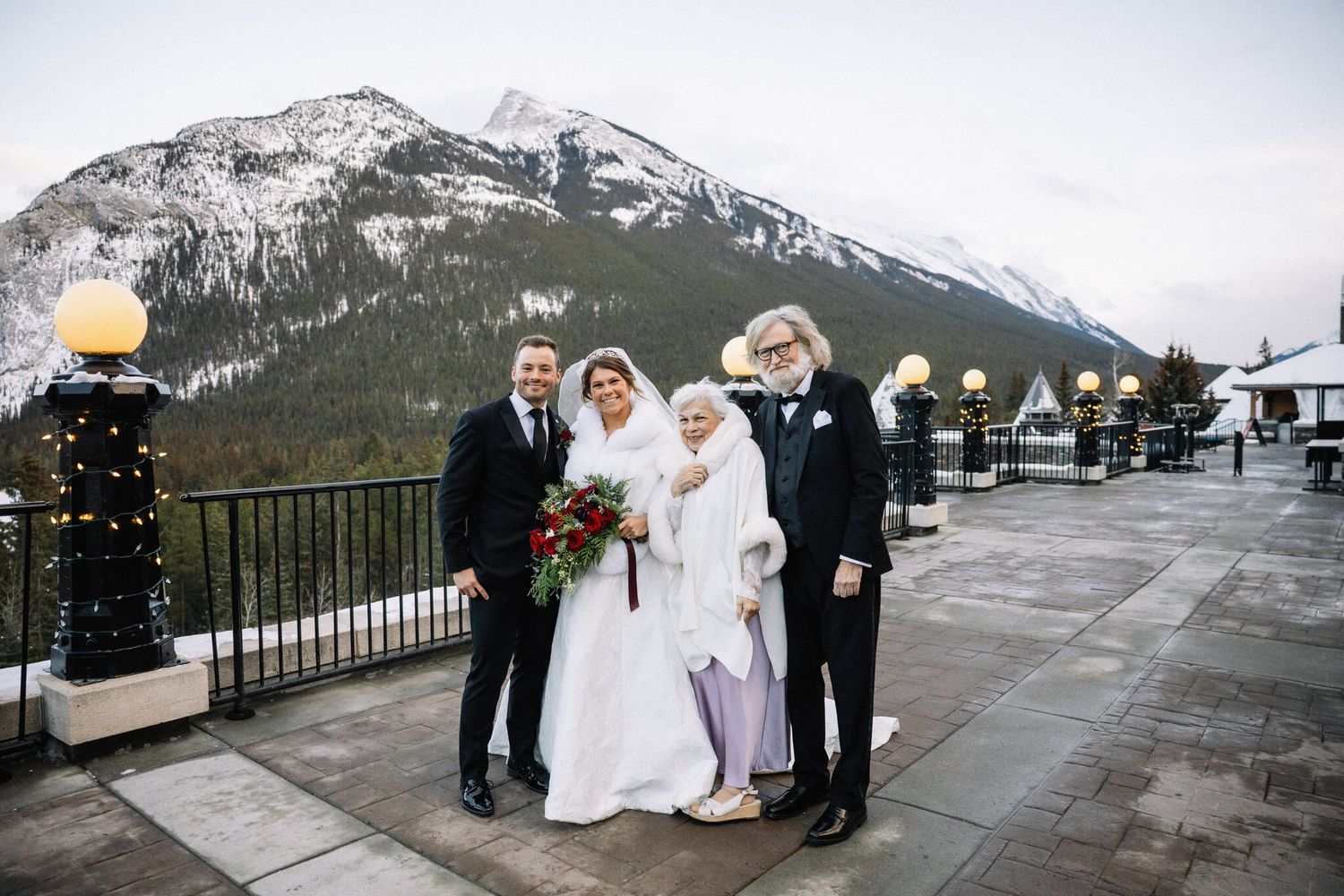 Bride and groom with two loved ones on a Fairmont Banff Springs terrace with a snowy mountain behind